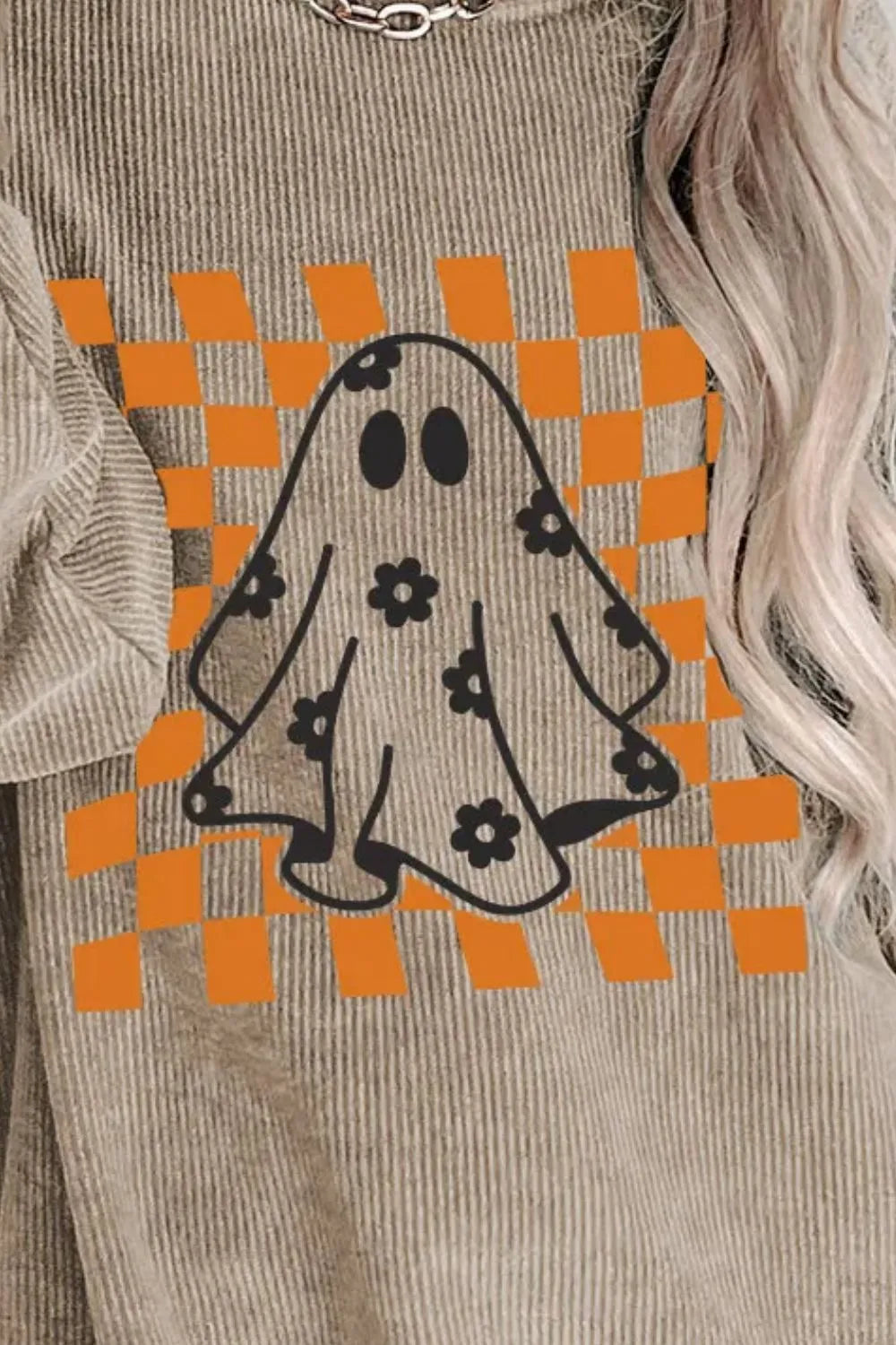 A person wears a beige corduroy long-sleeve sweatshirt with an orange checkered ghost design.