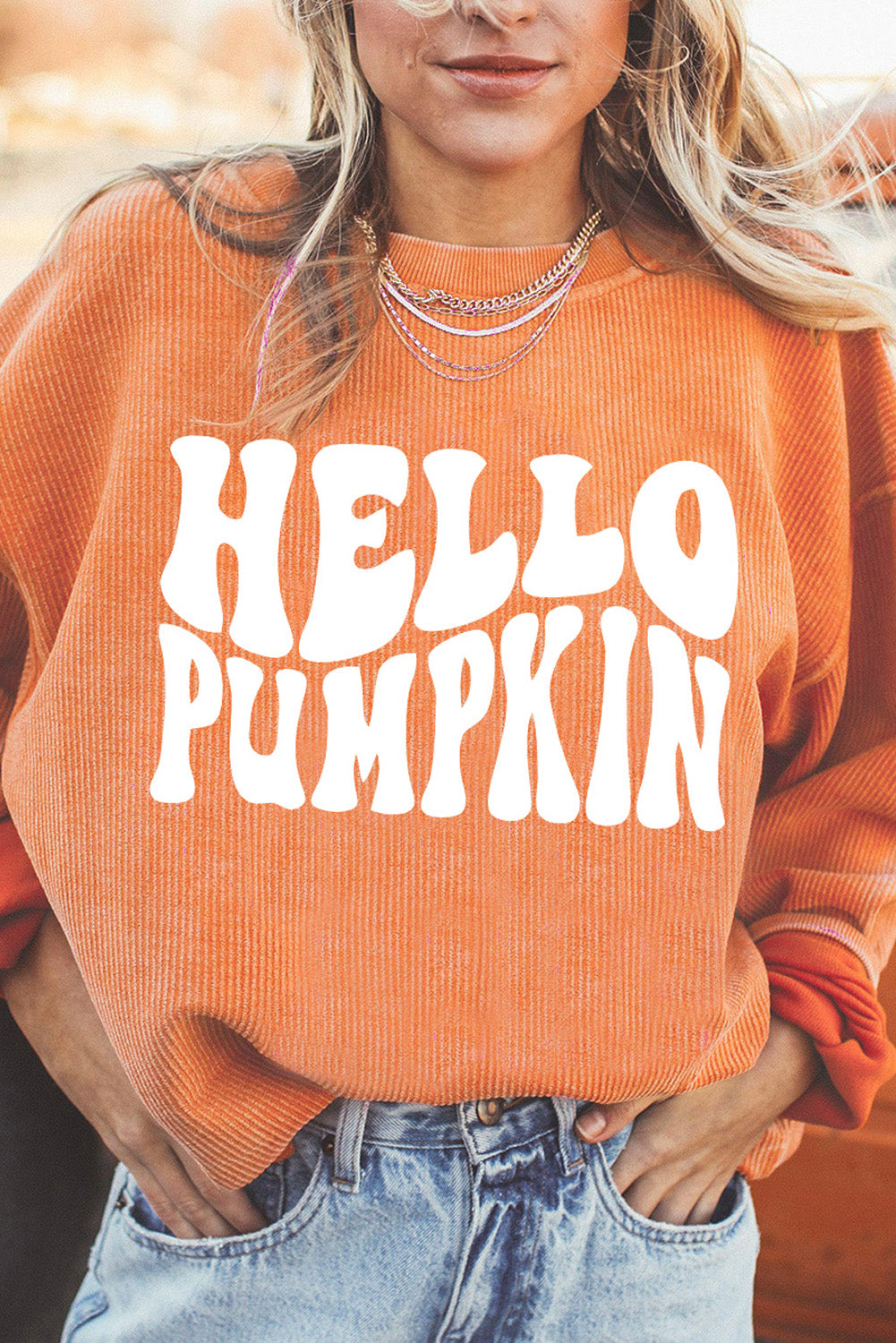 A woman wears an orange "HELLO PUMPKIN" graphic sweatshirt with blue jeans.