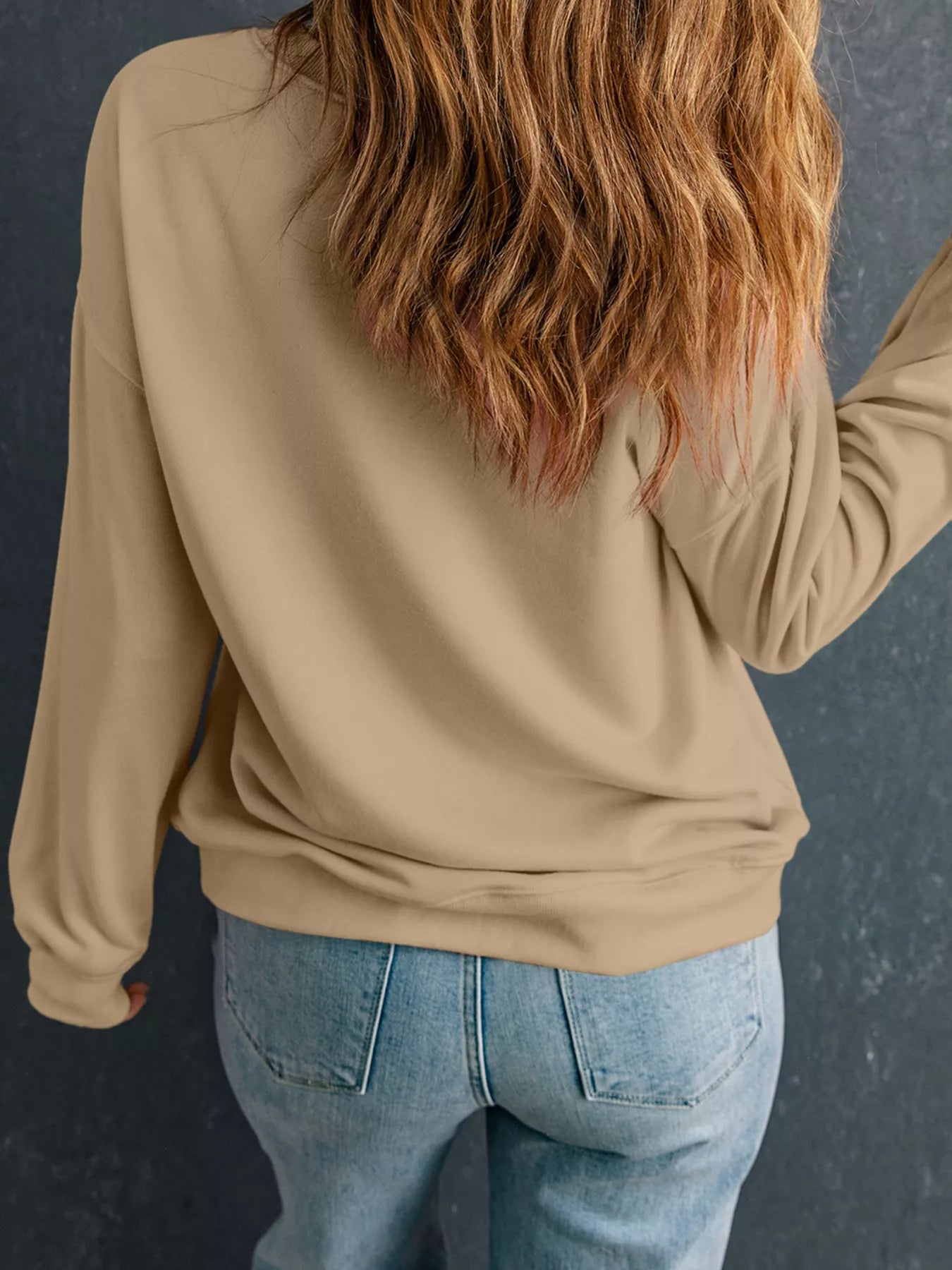 A woman from behind wears a beige drop shoulder sweatshirt and blue jeans.