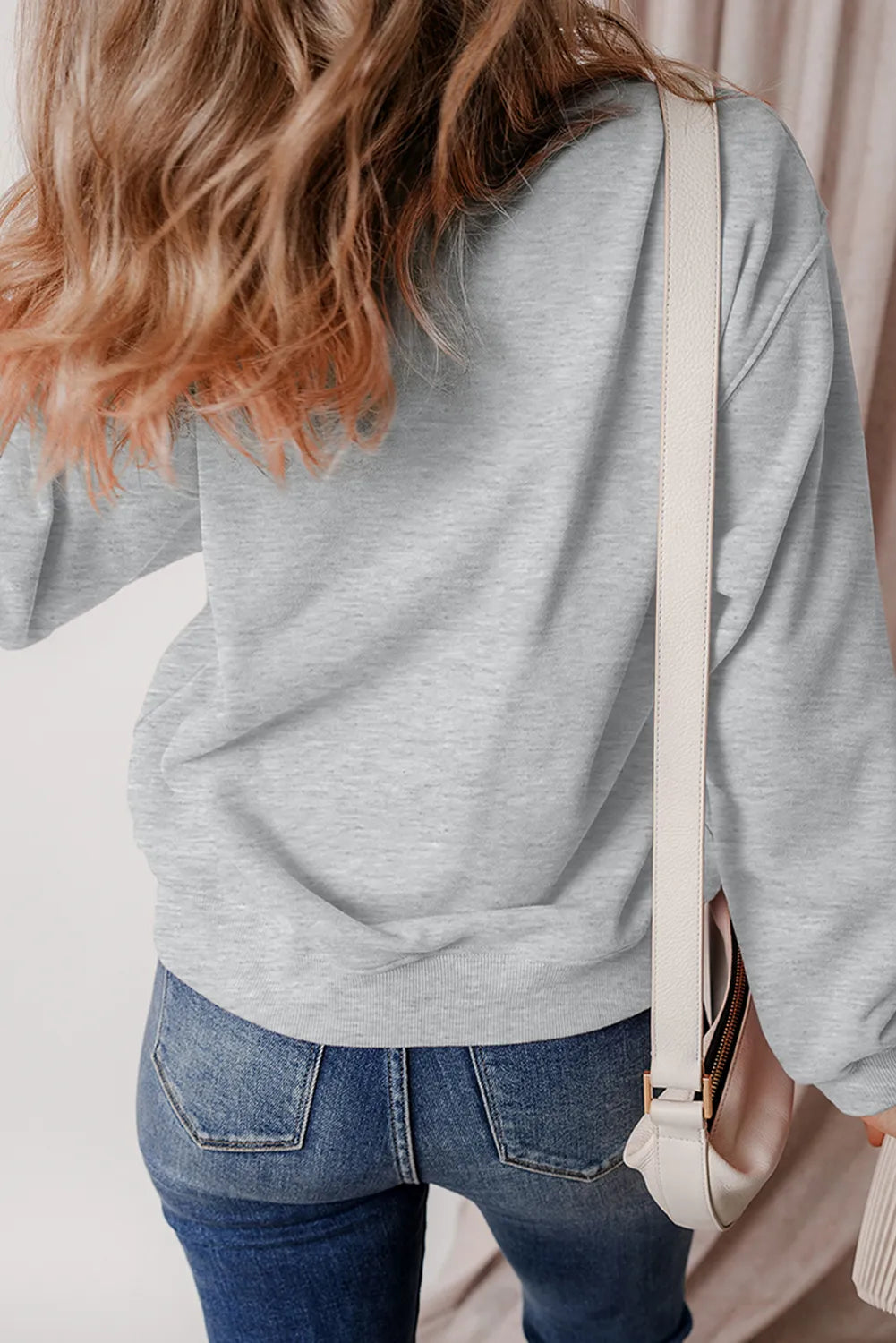 A woman from behind wears a gray long-sleeve sweatshirt and blue jeans.