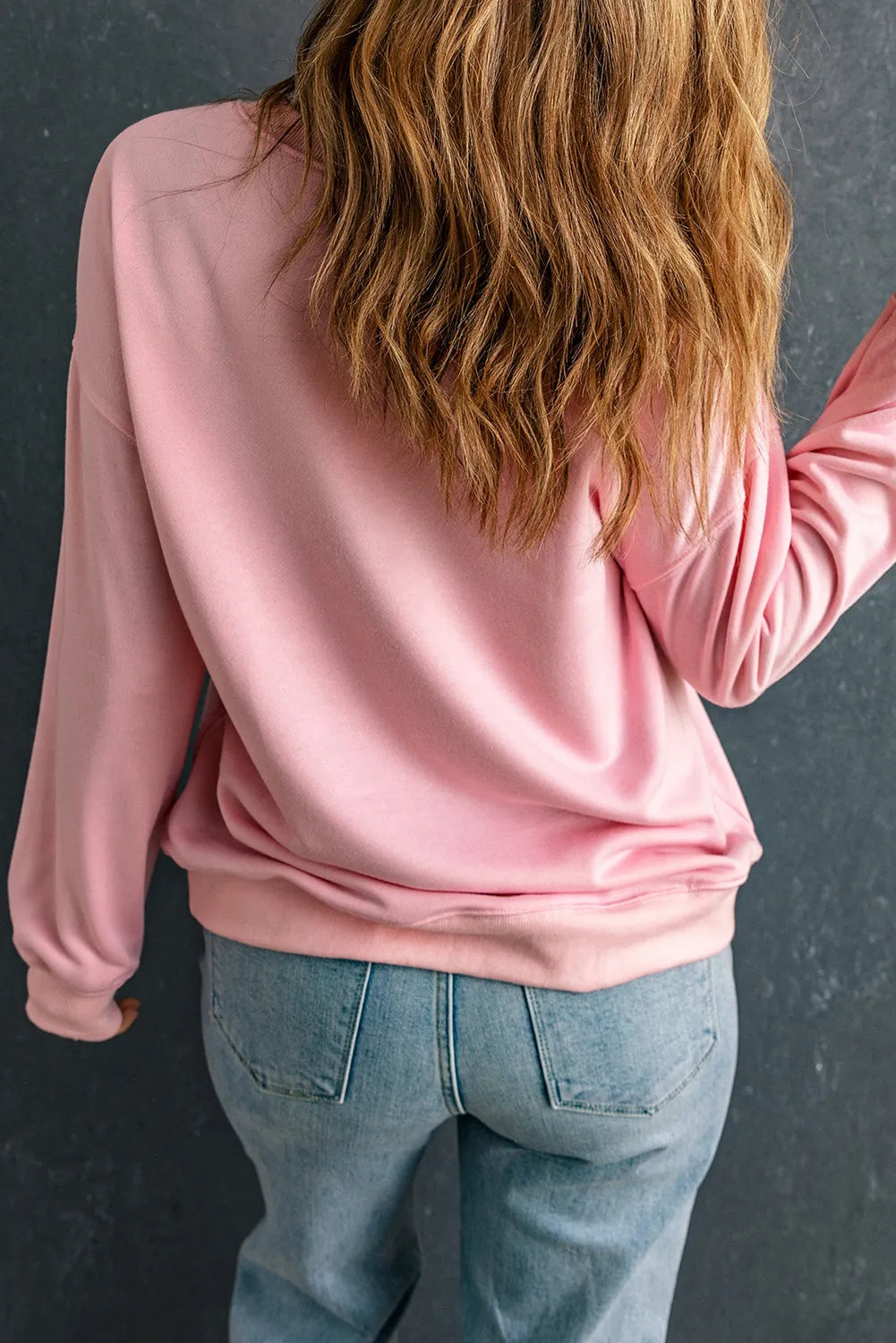 A woman from behind wears a pink long-sleeve sweatshirt and blue jeans.