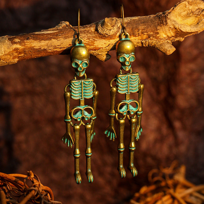 Two antique bronze skeleton earrings with teal accents hang from a branch.