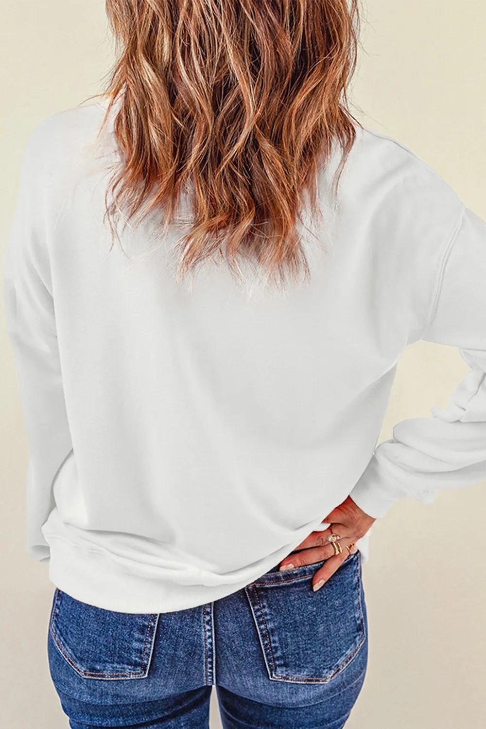 A woman from behind wears a white long-sleeve sweatshirt and blue jeans.