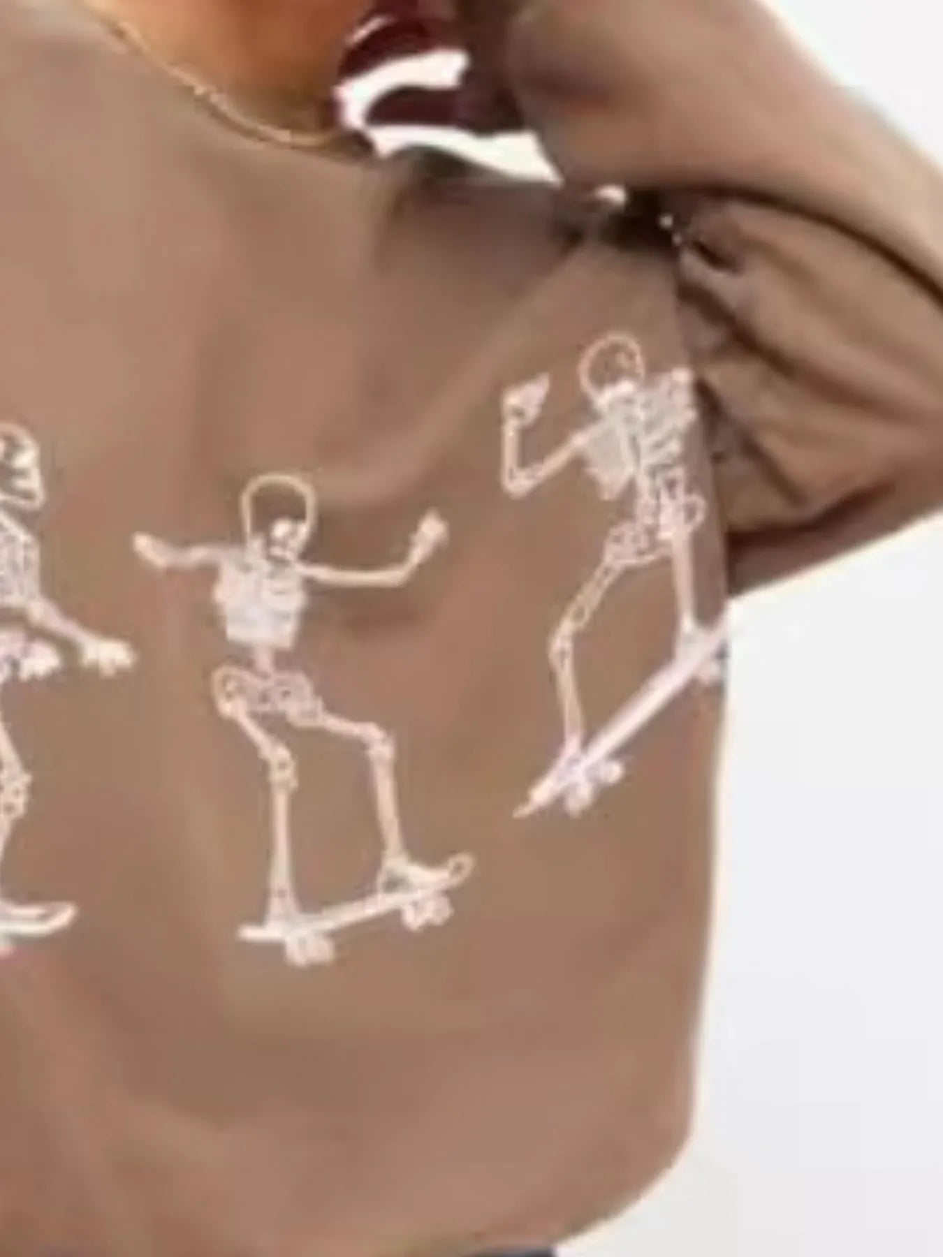 An oversized brown sweatshirt features three white skeleton graphics skateboarding.