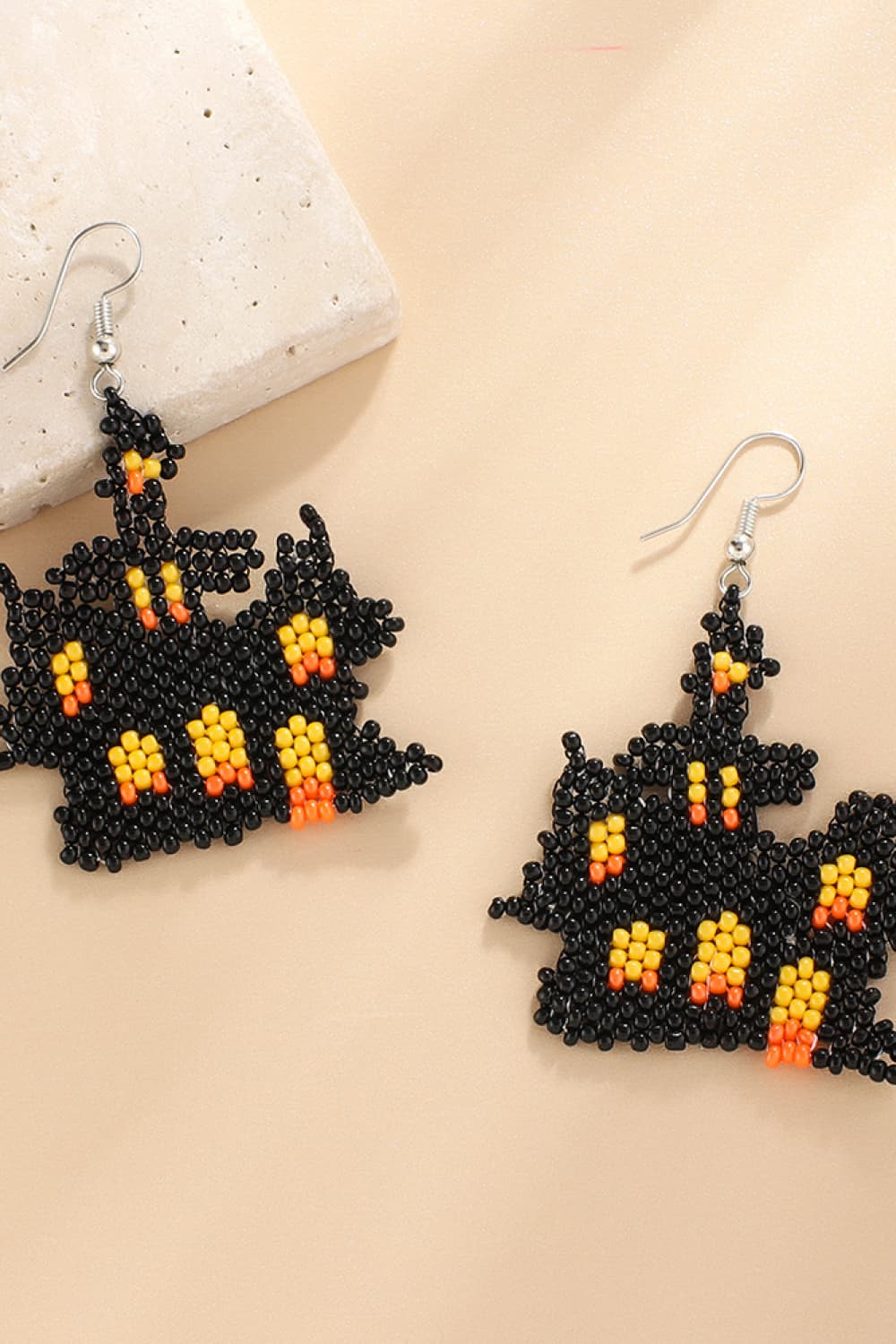 A pair of black, orange, and yellow beaded Halloween-themed haunted house earrings.