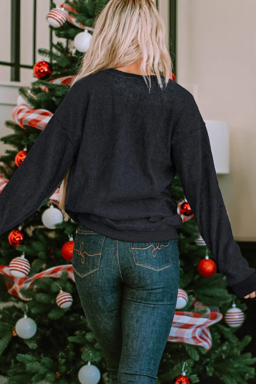 Woman in a black round neck sweatshirt and jeans, facing away from the camera.