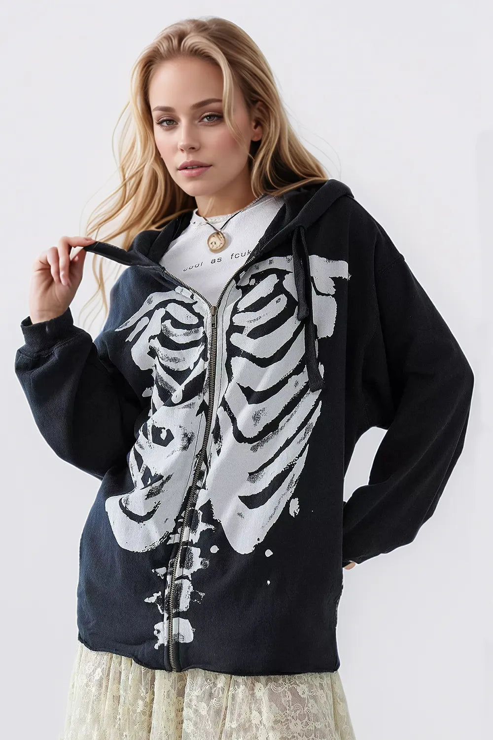 A woman wears a black skeleton zip-up drawstring hoodie over a white top and lace skirt.