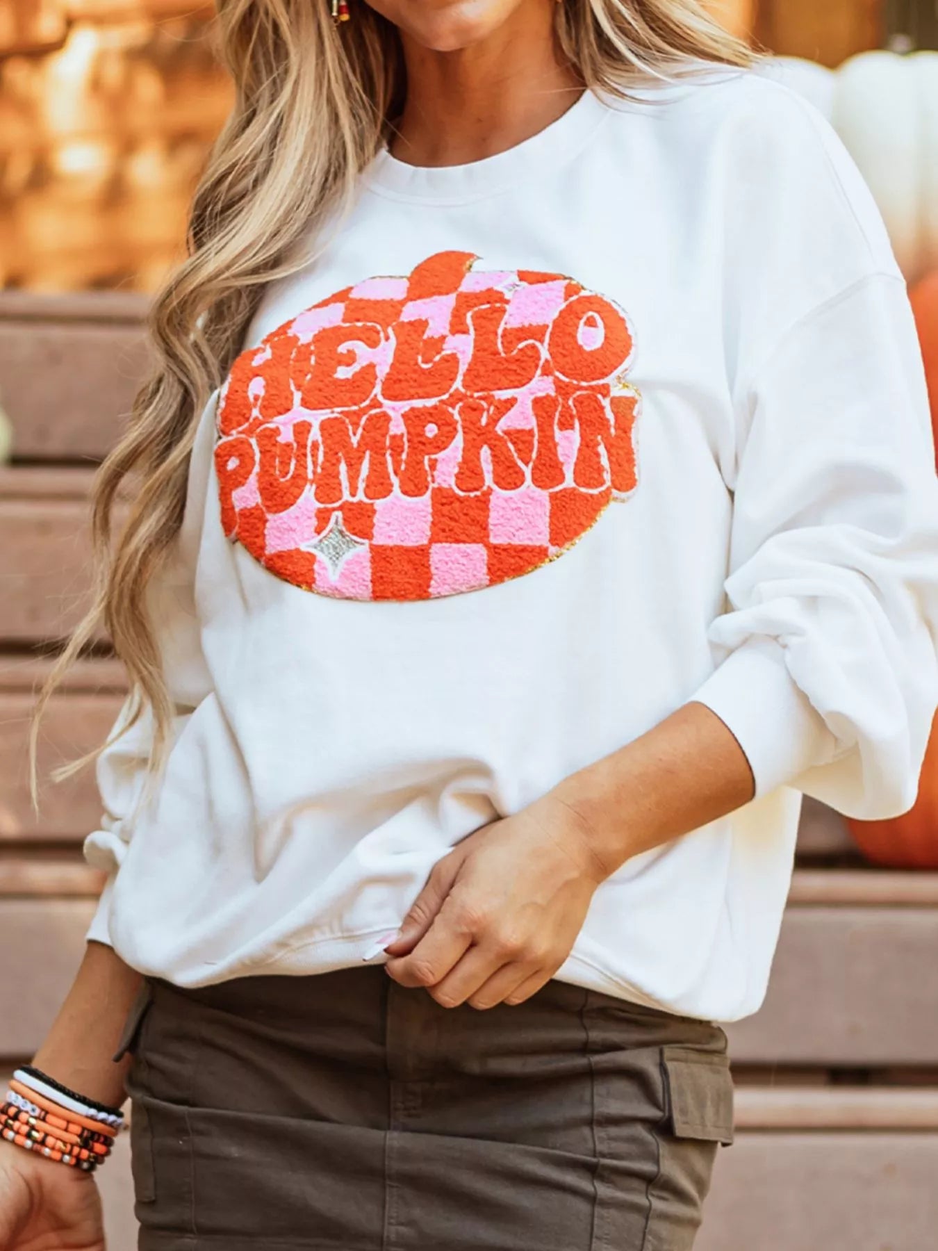 A woman wears a white long-sleeve sweatshirt with a "Hello Pumpkin" patch.