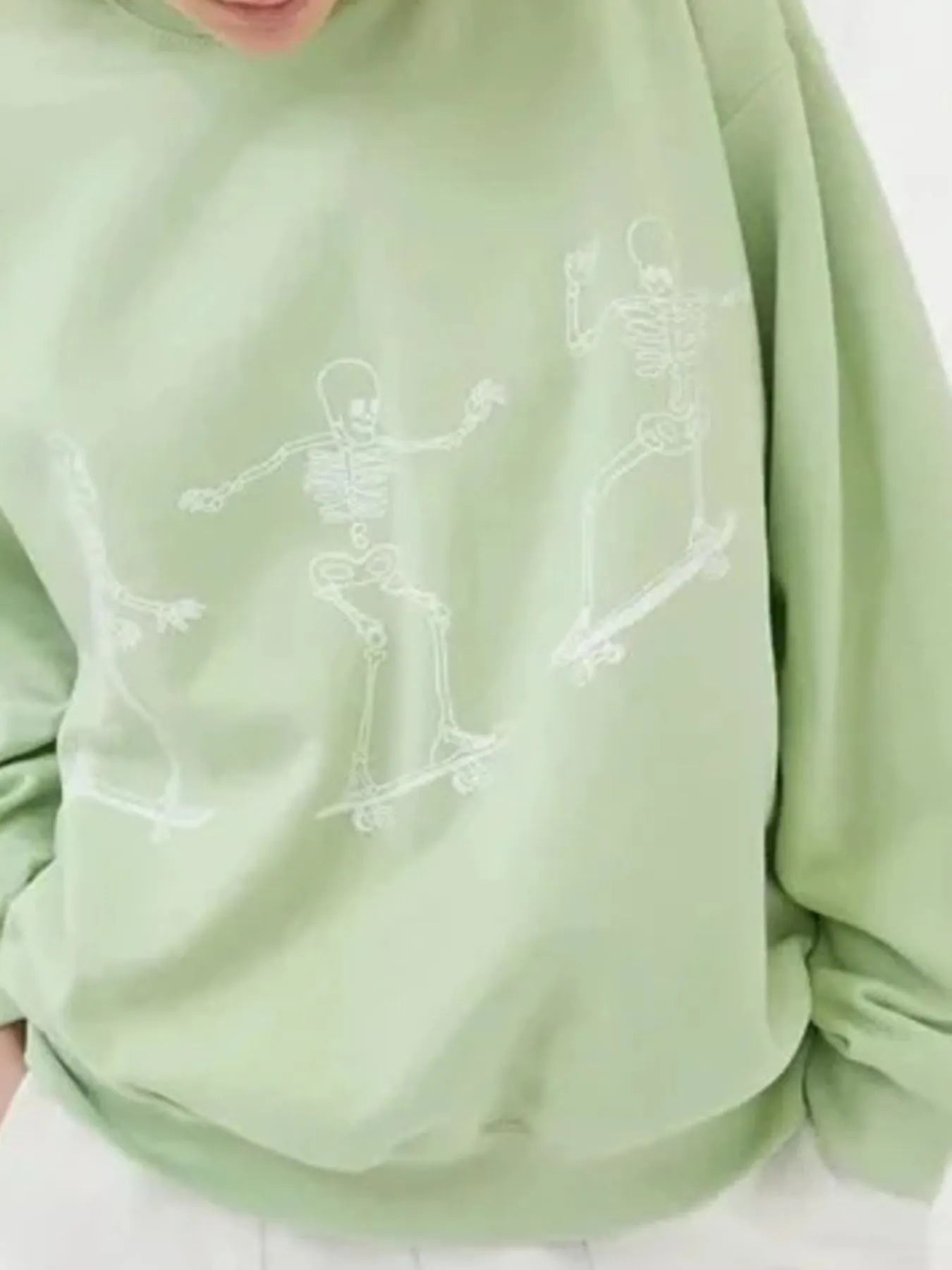 A light green oversized sweatshirt features three white skeleton graphics skateboarding.