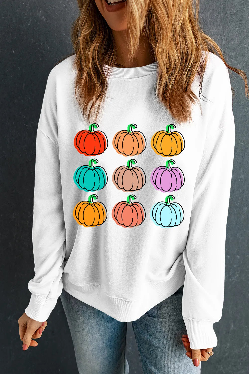 A woman wears a white long-sleeve sweatshirt with a colorful pumpkin graphic.