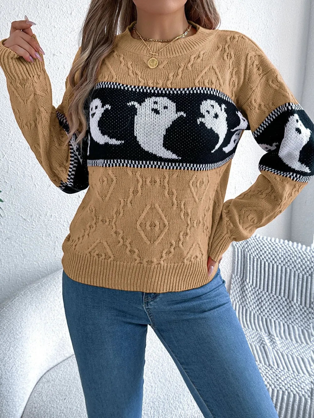 A woman wears a tan long-sleeve sweater with a black and white ghost pattern.