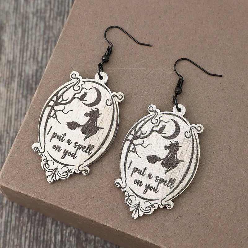 A pair of wooden dangle earrings featuring a witch on a broomstick and the phrase "I put a spell on you."