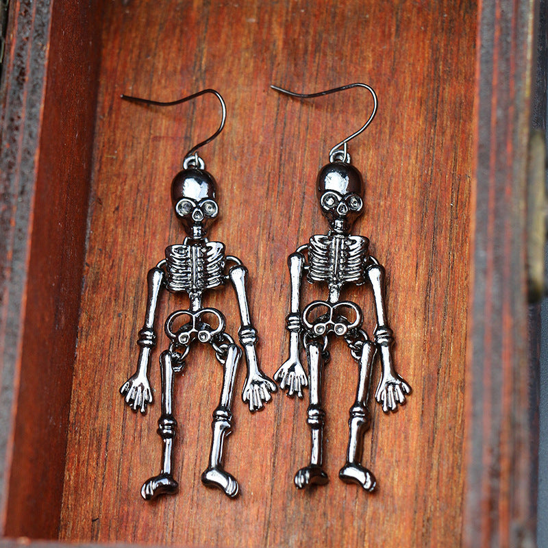 Two dark silver-toned skeleton alloy earrings hang against a wooden background.