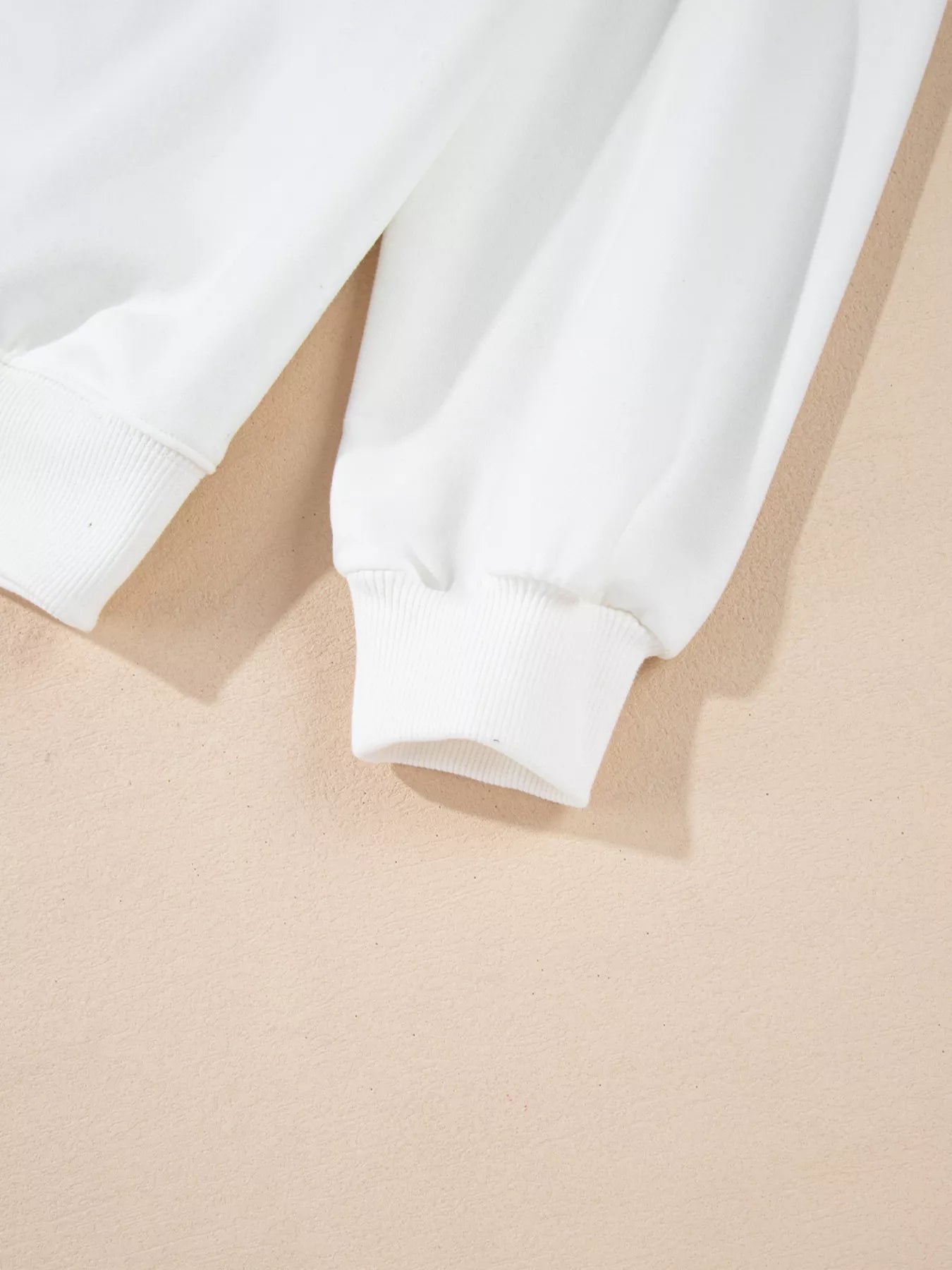 Close-up of a white long-sleeve sweatshirt with ribbed cuffs.