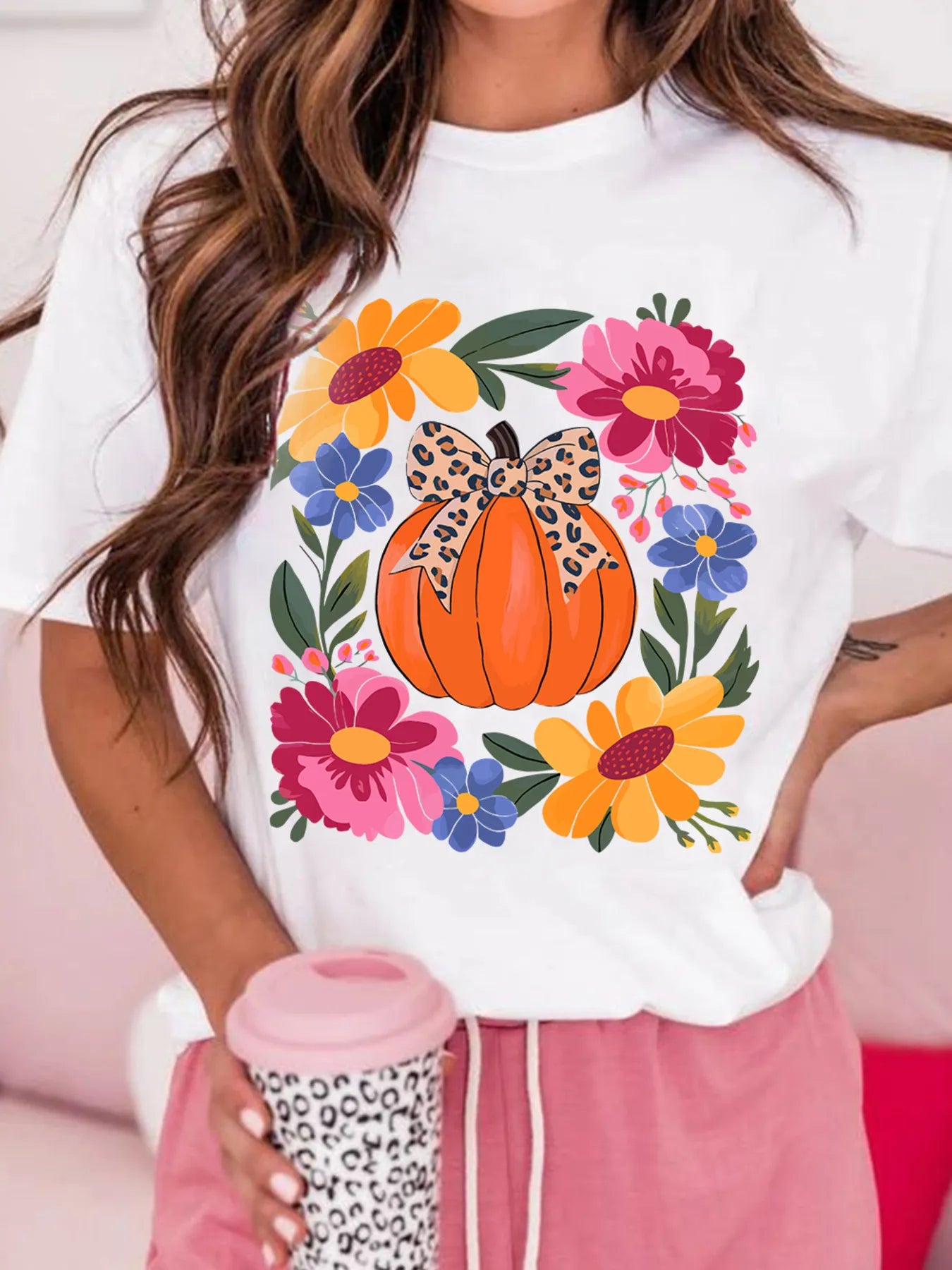 A woman wears a white t-shirt with a pumpkin and floral graphic.