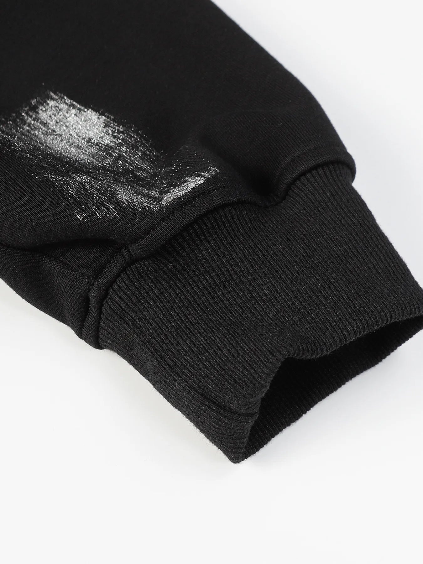 Close-up of a black hoodie sleeve with a silver graffiti print and ribbed cuff.