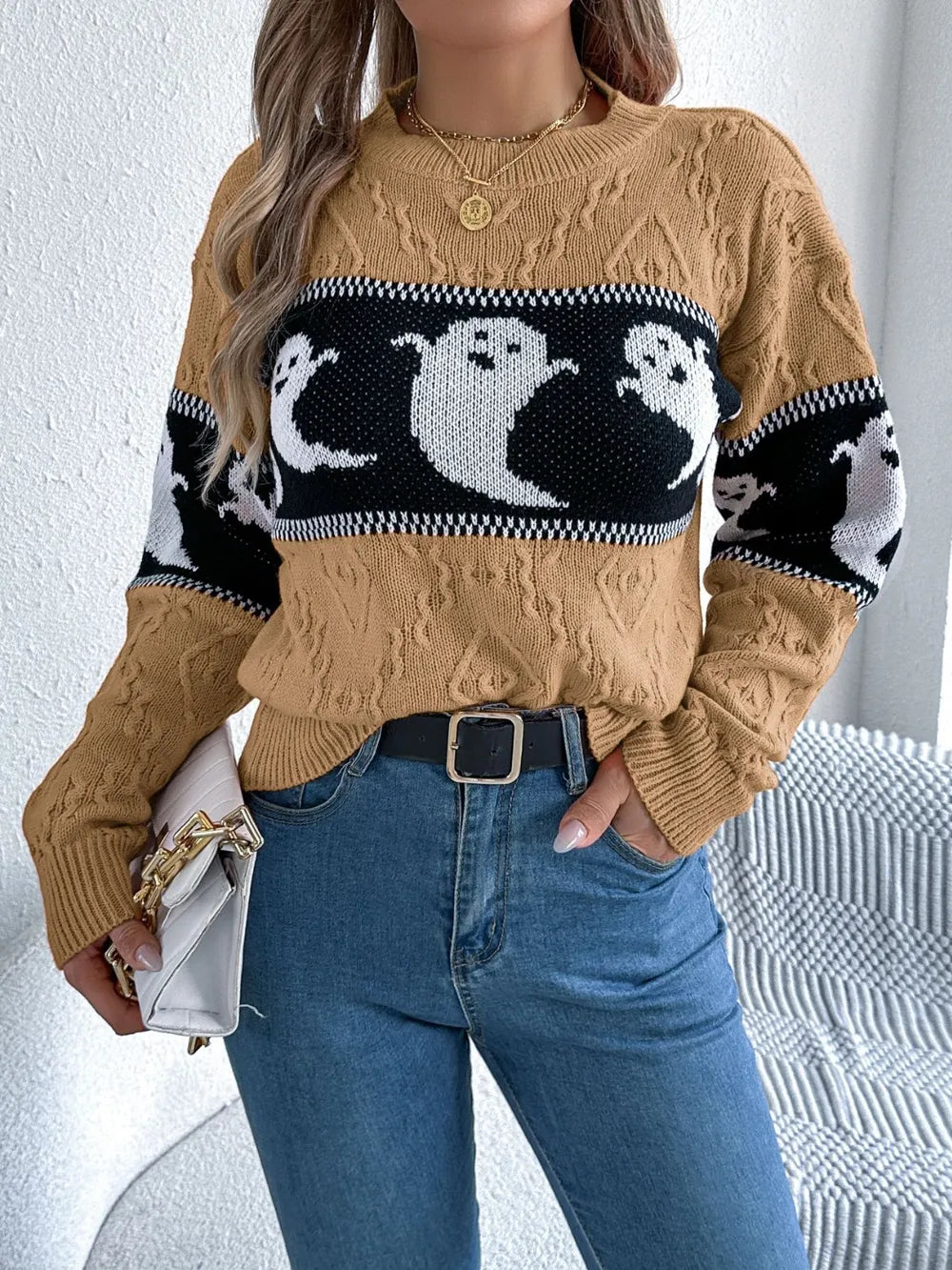 A woman wears a tan, long-sleeve sweater with a black and white ghost pattern.
