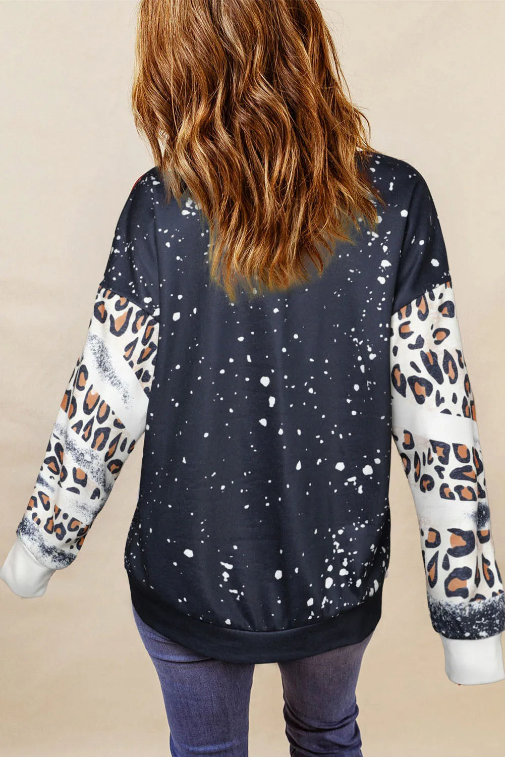 A woman from behind wears a black sweatshirt with white paint splatters and leopard print sleeves.