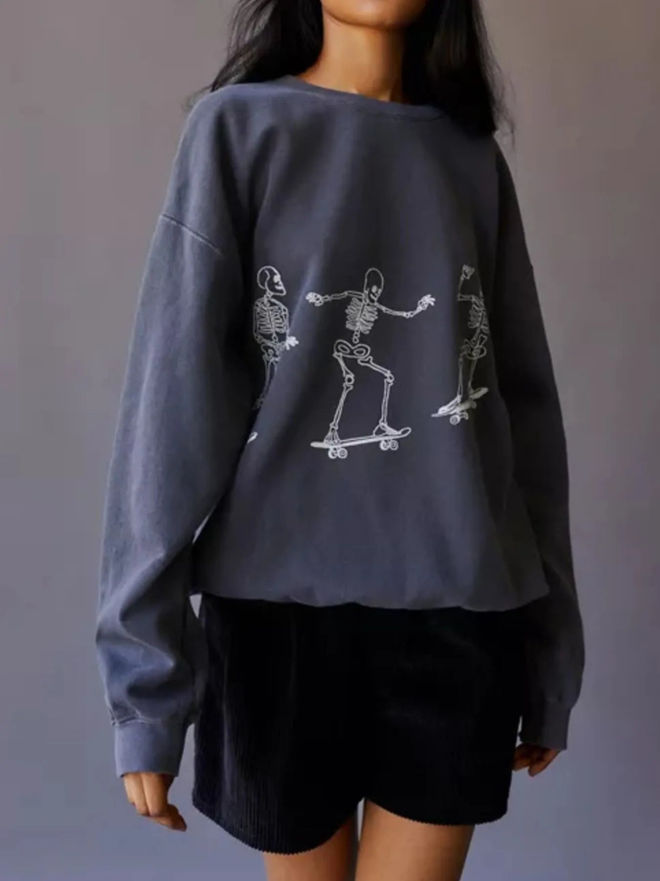 Oversized gray sweatshirt with white skeleton graphics skateboarding.