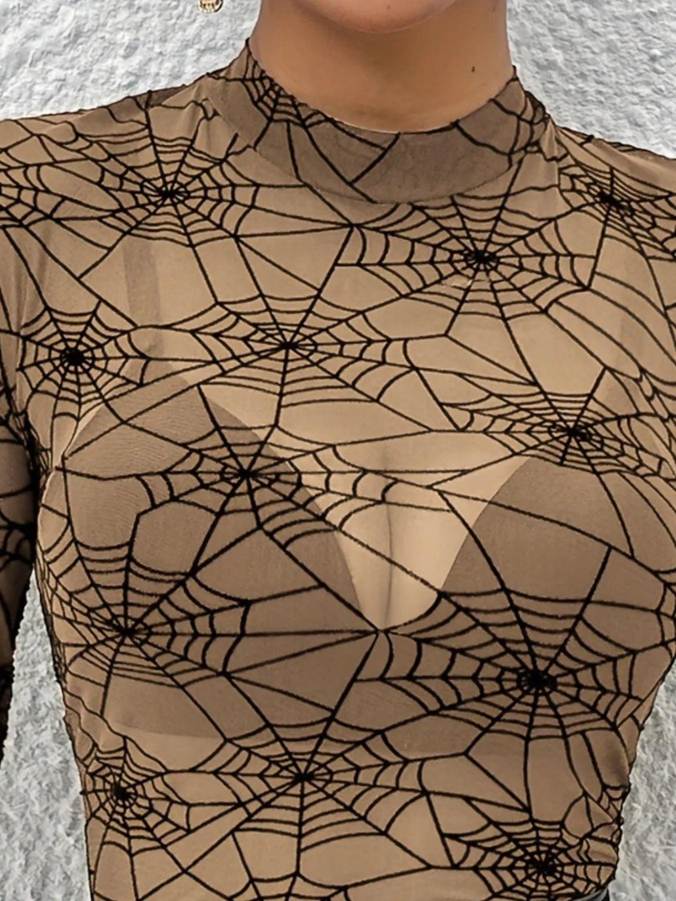 A sheer, long-sleeve blouse with a black spider web print on a tan background.