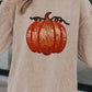 A woman wears a beige long-sleeve sweatshirt with a sequin pumpkin design.