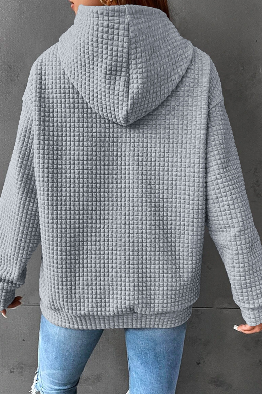 A person from behind wearing a gray waffle knit hoodie and blue jeans.