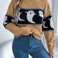 A woman wears a brown, black, and white ghost-patterned long-sleeve sweater with jeans.