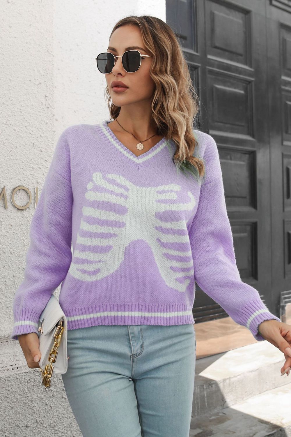 A woman wears a purple V-neck sweater with a white skeleton pattern.