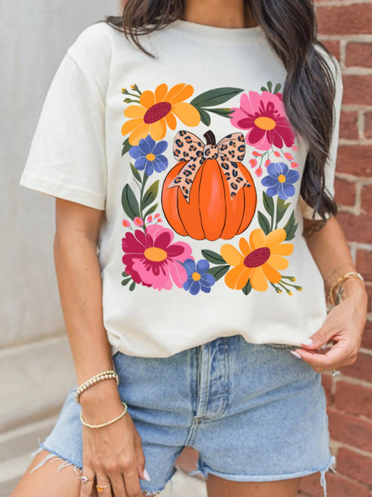 A woman wears a white t-shirt with a pumpkin and floral graphic.