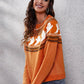 A woman smiles while wearing an orange ghost pattern round neck long sleeve sweater.