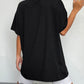 A woman from behind wearing a black round neck short sleeve t-shirt and white shorts.
