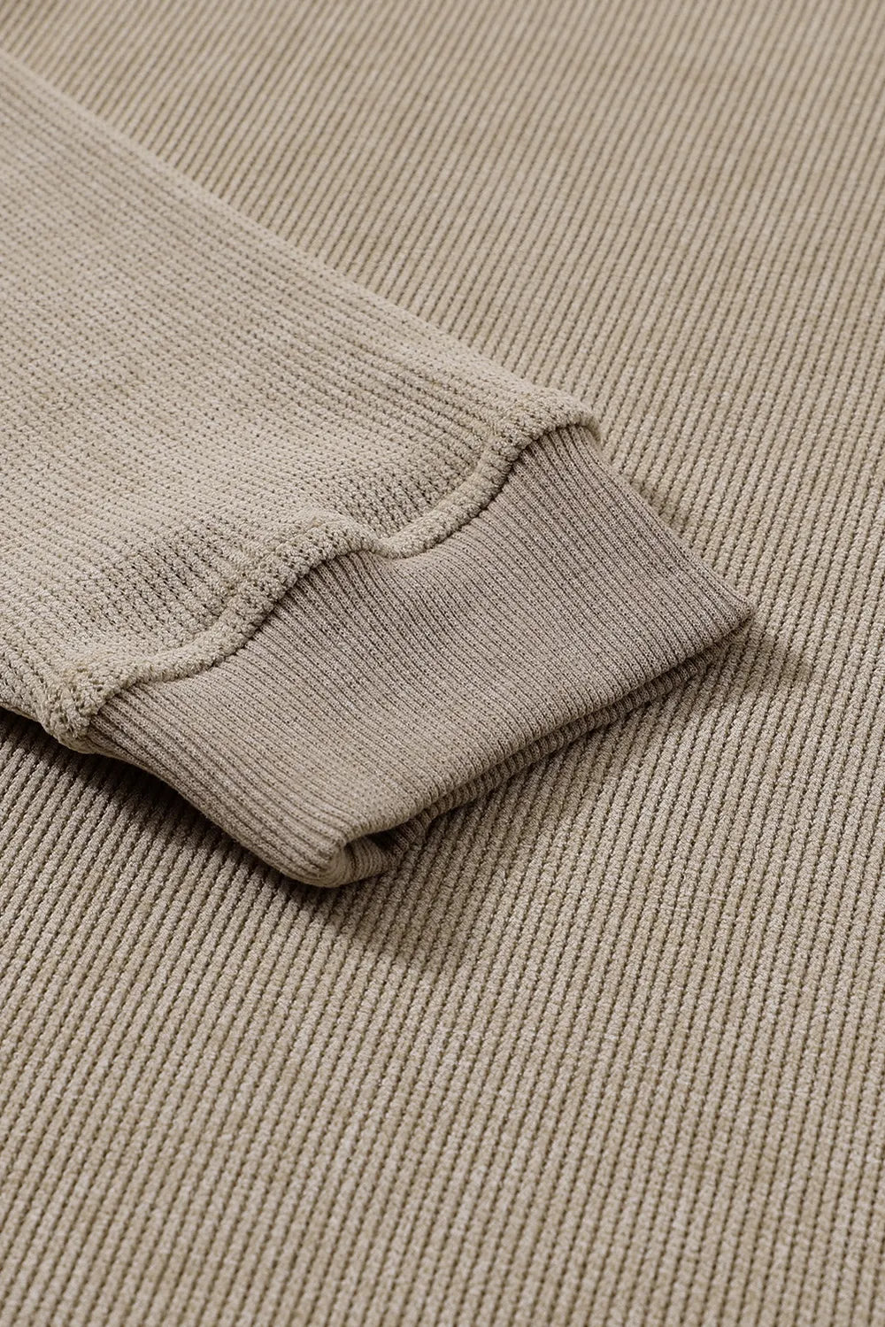 Close-up of a beige long-sleeve sweatshirt with ribbed cuffs and textured fabric.