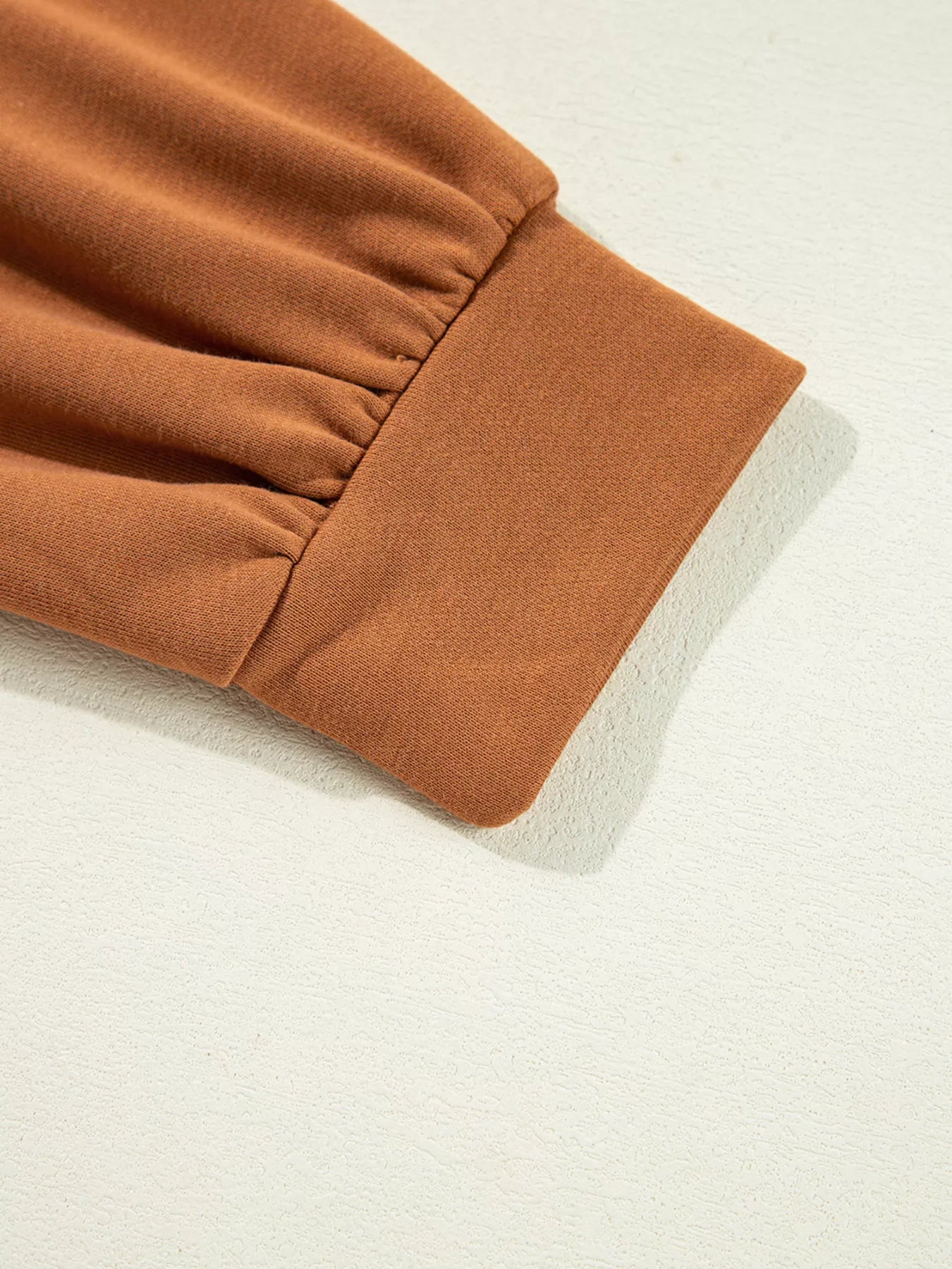 Close-up of a brown long-sleeve top with gathered fabric at the cuff.