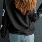A woman from behind wears a black long-sleeve sweatshirt with iridescent ghost appliques.