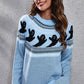 A woman smiles while wearing a light blue ghost pattern round neck long sleeve sweater.