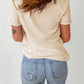 A woman from behind wears a beige short-sleeve t-shirt and light blue ripped jeans.