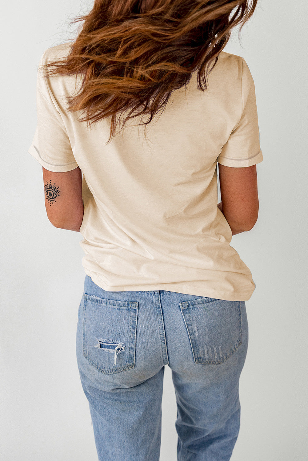 A woman from behind wears a beige short-sleeve t-shirt and light blue ripped jeans.