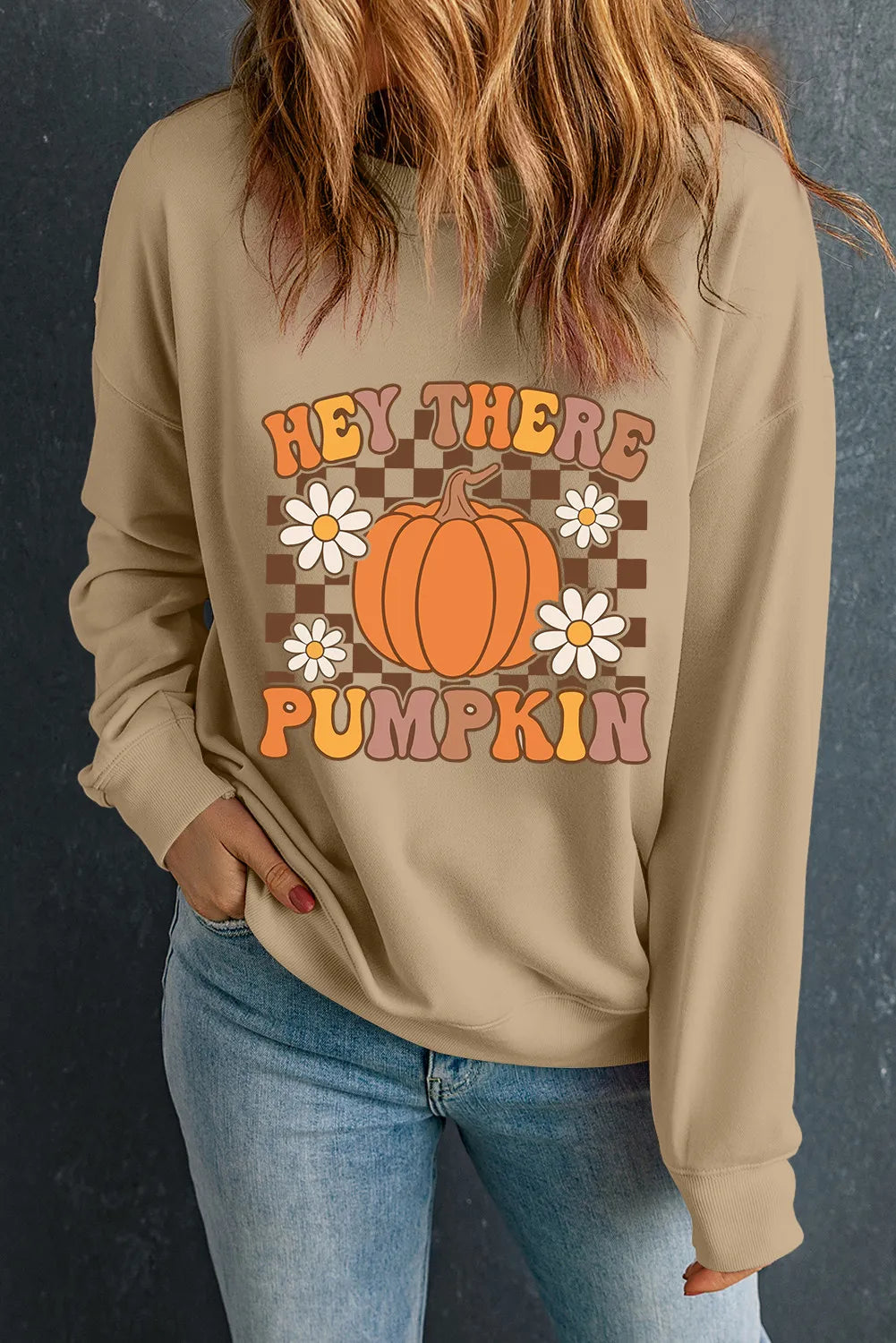 A woman wears a tan long-sleeve sweatshirt with a "Hey There Pumpkin" graphic.