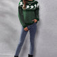 A woman models a green ghost pattern round neck long sleeve sweater with jeans and boots.