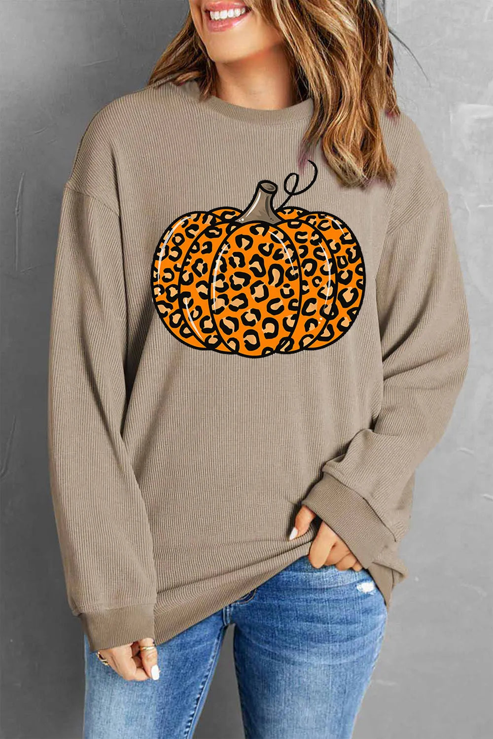 A woman wears a long-sleeve, round-neck sweatshirt with a leopard print pumpkin graphic.