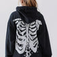 A person from behind wears a black skeleton zip-up hoodie over a lace skirt.