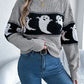 A woman wears a gray, long-sleeve sweater with a black and white ghost pattern.