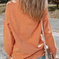 A woman from behind wears an orange ribbed round neck sweatshirt and jeans.
