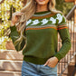 A woman models a green long-sleeve sweater with white ghost patterns and a denim skirt.