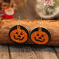 A pair of orange glitter pumpkin earrings with black accents rests on a wooden log.