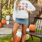 A woman wears a white long-sleeve sweatshirt with a pumpkin graphic and a denim skirt.