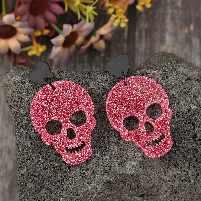 A pair of pink glitter skull earrings with black heart-shaped studs.