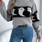 A woman wears a gray long-sleeve sweater with a black and white ghost pattern.