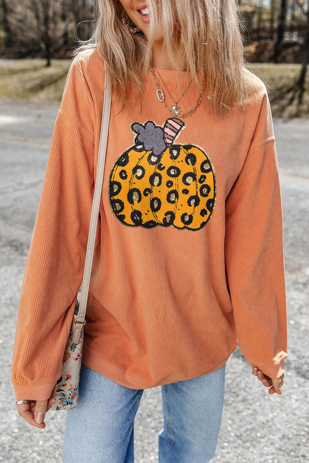 A woman wears an orange corduroy sweatshirt with a leopard print pumpkin design.