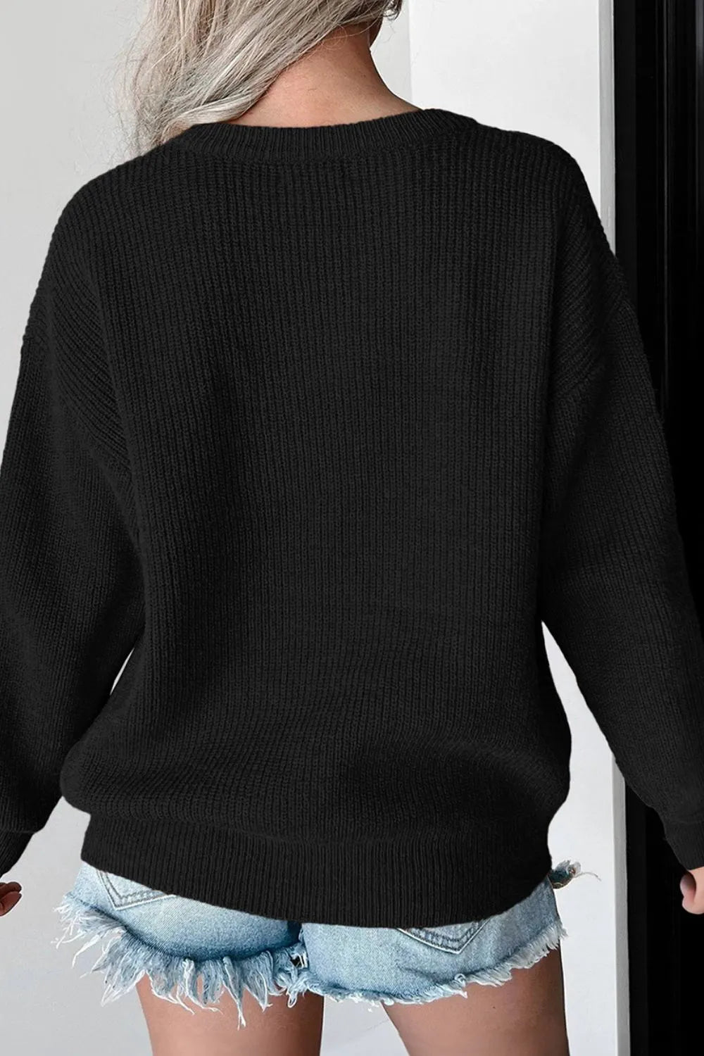 A woman from behind wears a black long-sleeve round-neck sweater and denim shorts.
